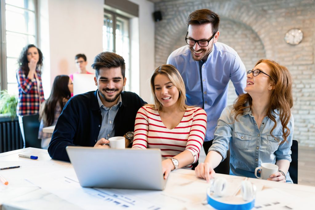 4 people sit at a desk looking at a laptop enthusiastically